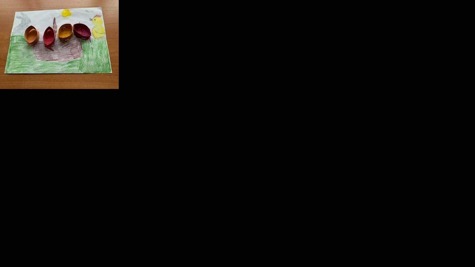 Kartka wielkanocna wykonana kredkami z dużym brązowym koszyczkiem wielkanocnym, przyklejonymi i namalowanymi farbami czterema pisankami (pomarańczowa, żółta, czerwona i bordowa), z lewej strony znadjuje się szary zajączek, z prawej żółty kurczaczek, koszyczek jest ustawiony na zielonej trawie. Autor: Maciej A.