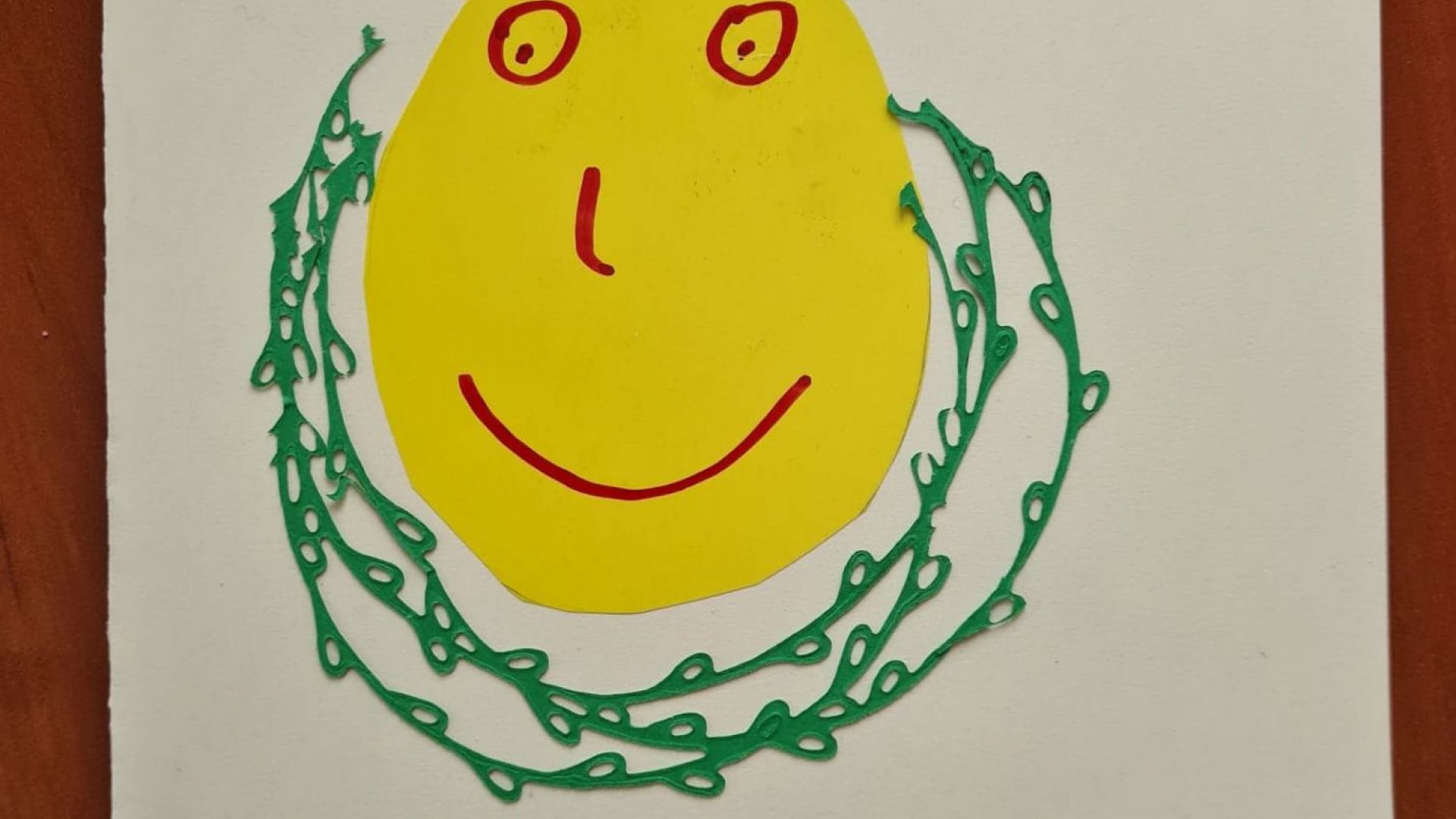 Kartka wielkanocna z naklejoną na środku żółtą pisanką z uśmiechniętą buzią w otoczeniu zielonych gałązek, z napisem wesołych świąt oraz wesołego jajka i smacznego śniadanka. Autor: Magda D.