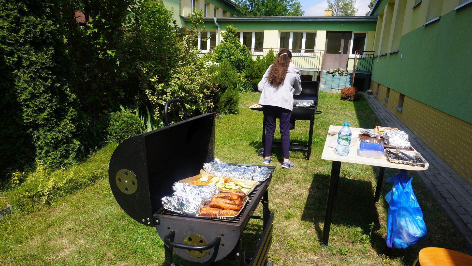 Grill, na którym pieką się kiełbaski, kaszanki i warzywa.