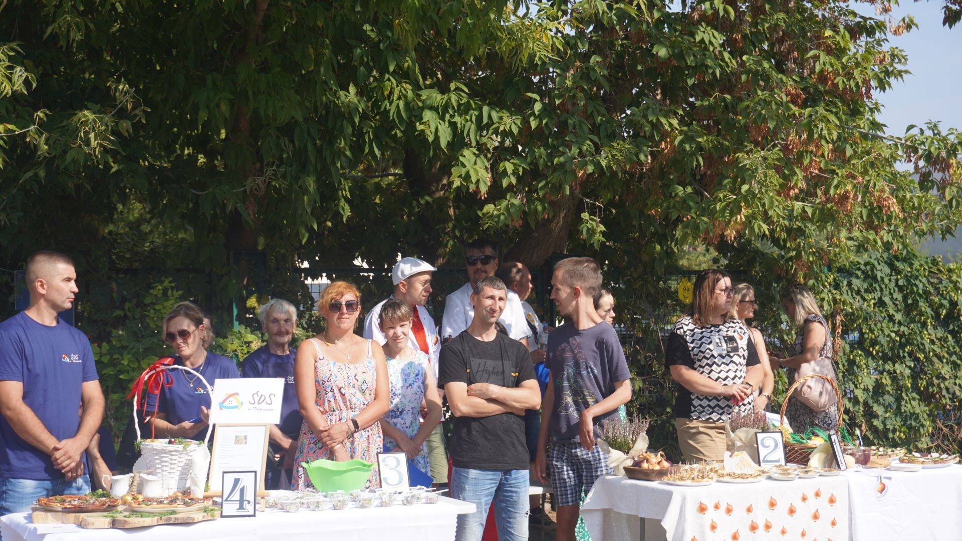 Uczestnicy spotkania ''Dzień Cebuli'' stoją przy stołach z potrawami z cebuli.