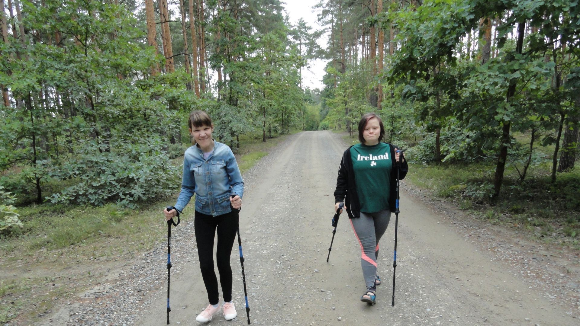 Uczestniczki Małgosia i Marta maszerują leśną ścieżką z kijkami nordic walking.