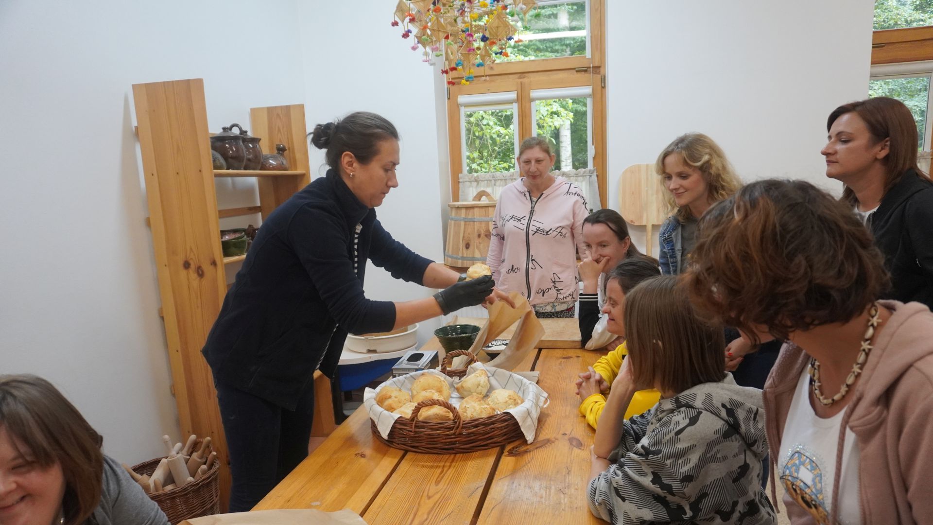 Pani prowadząca warsztaty ''Od ziarenka do bochenka'' w Muzeum Wsi Radomskiej, rozdaje uczestnikom upieczone bułki. 