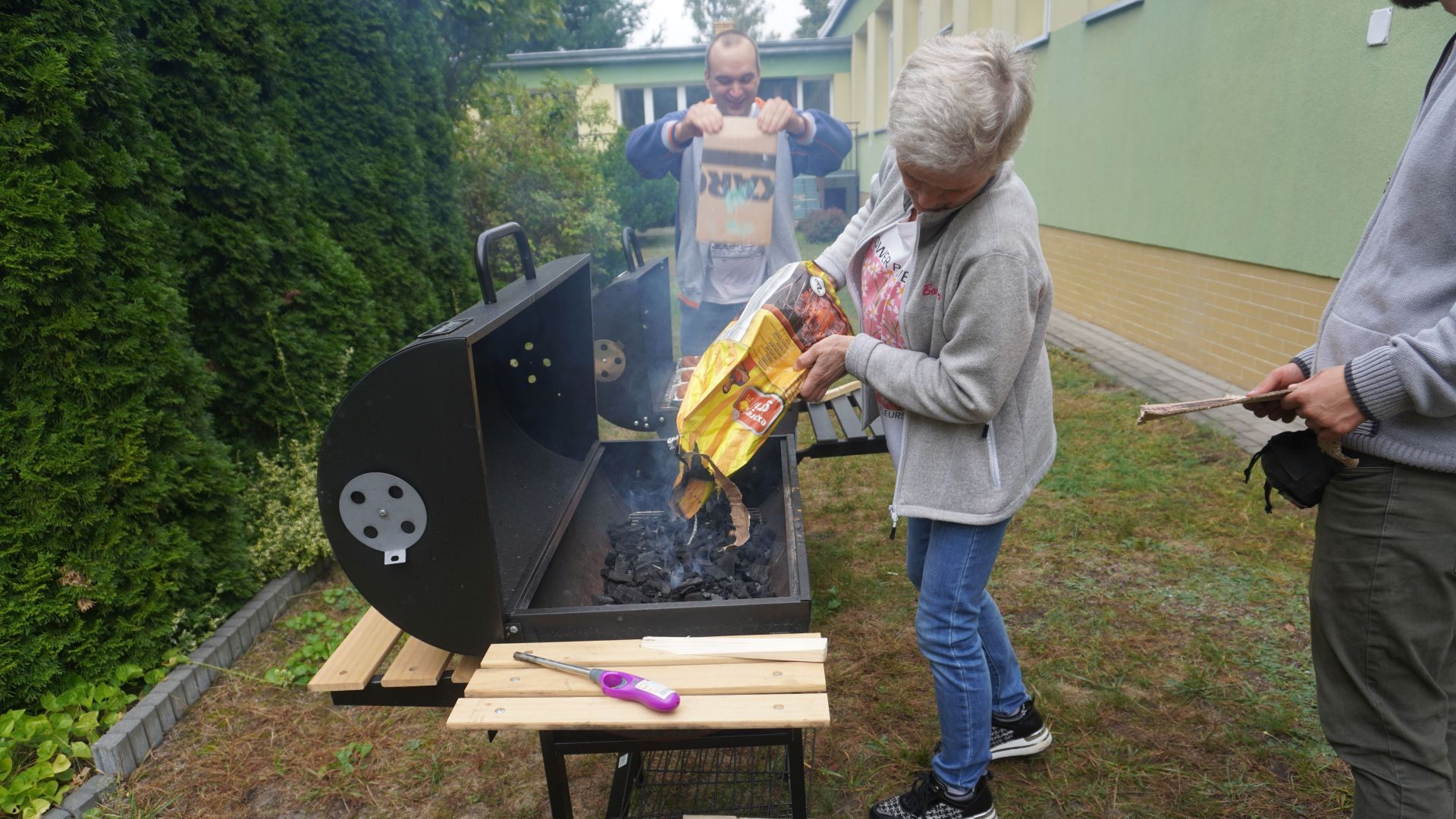 Uczestnicy z opiekunem rozpalają grille w ogrodzie z okazji Dnia Pieczonego Ziemniaka. 