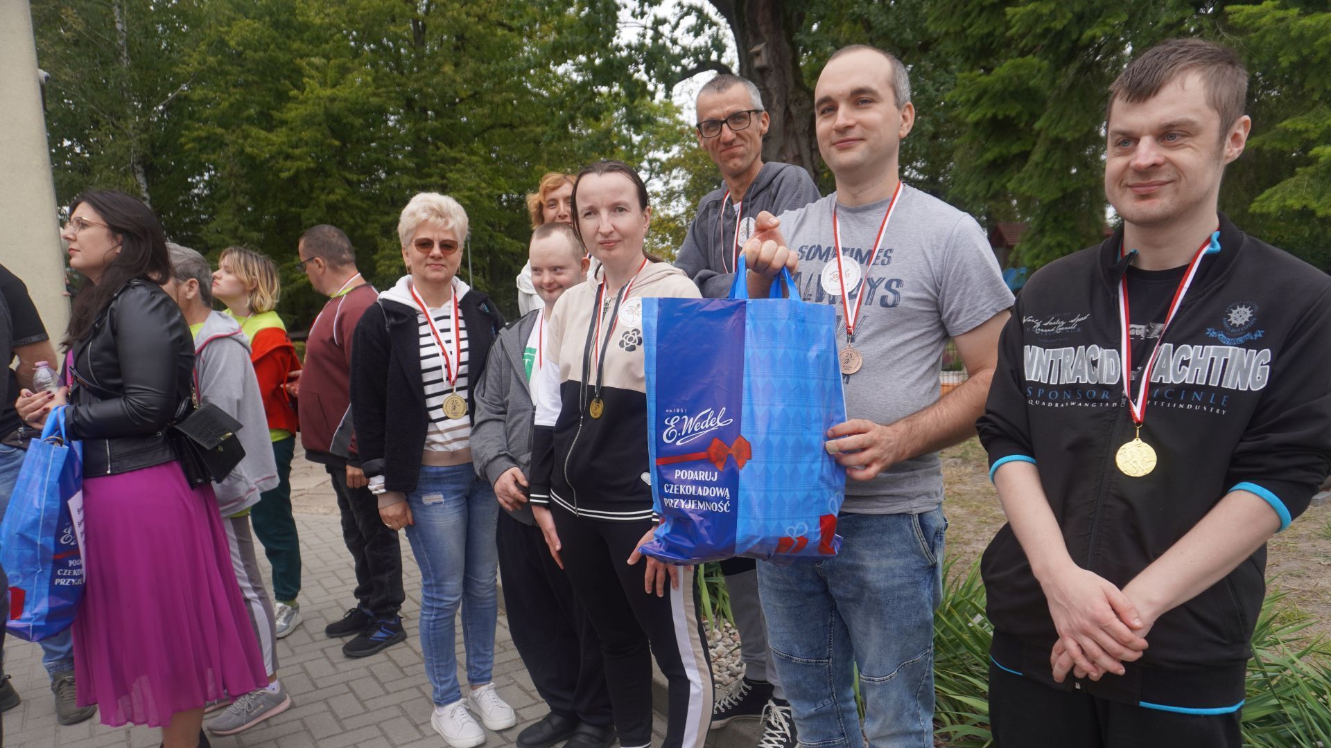 Uczestnicy wspólnie z terapeutą pozują do zdjęcia z nagrodami podczas XXV Powiatowych Jesiennych Biegów Przełajowych w Ignacowie.  