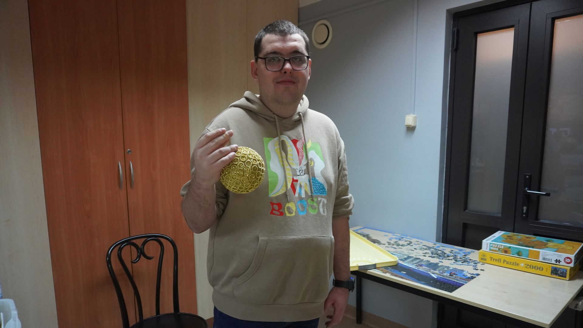 Uczestnik Karol trzyma w ręku złotą bombkę, którą zawiesi na choince.