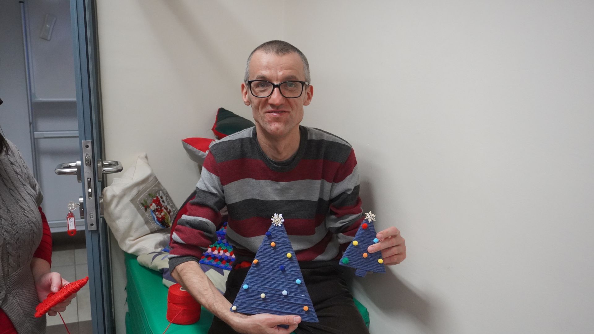Uczestnik Grzegorz pozuje do zdjęcia z ozdobami bożonarodzeniowymi, wykonanymi podczas warsztatów świątecznych. 