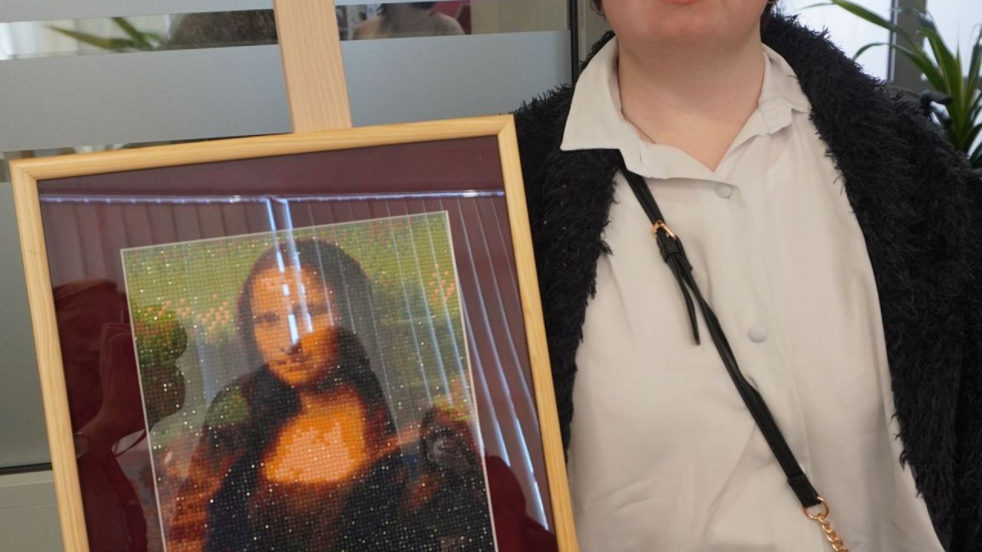 Anna M. pozuje do zdjęcia na tle wykonanej przez siebie pracy podczas wernisażu ''Sztuka-moja pasja''. 
