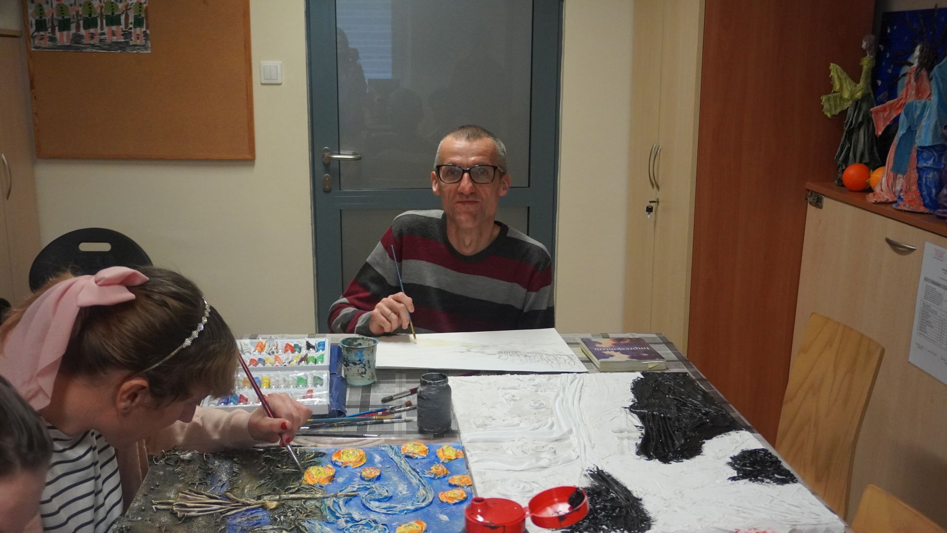 Artysta Grzegorz pozuje do zdjęcia podczas warsztatów plastycznych, na których maluje pracę farbą akrylową.