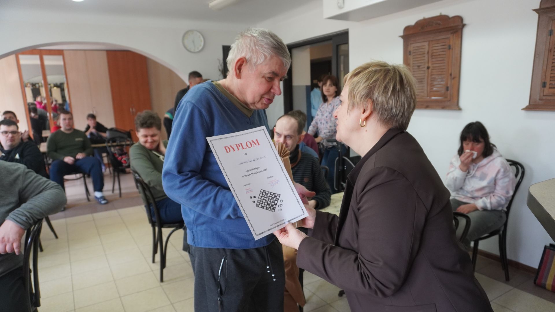 Pani dyrektor Justyna Juszczak wręcza panu Sławomirowi dyplom za zajęcie III miejsca w Turnieju warcabowym 2025.