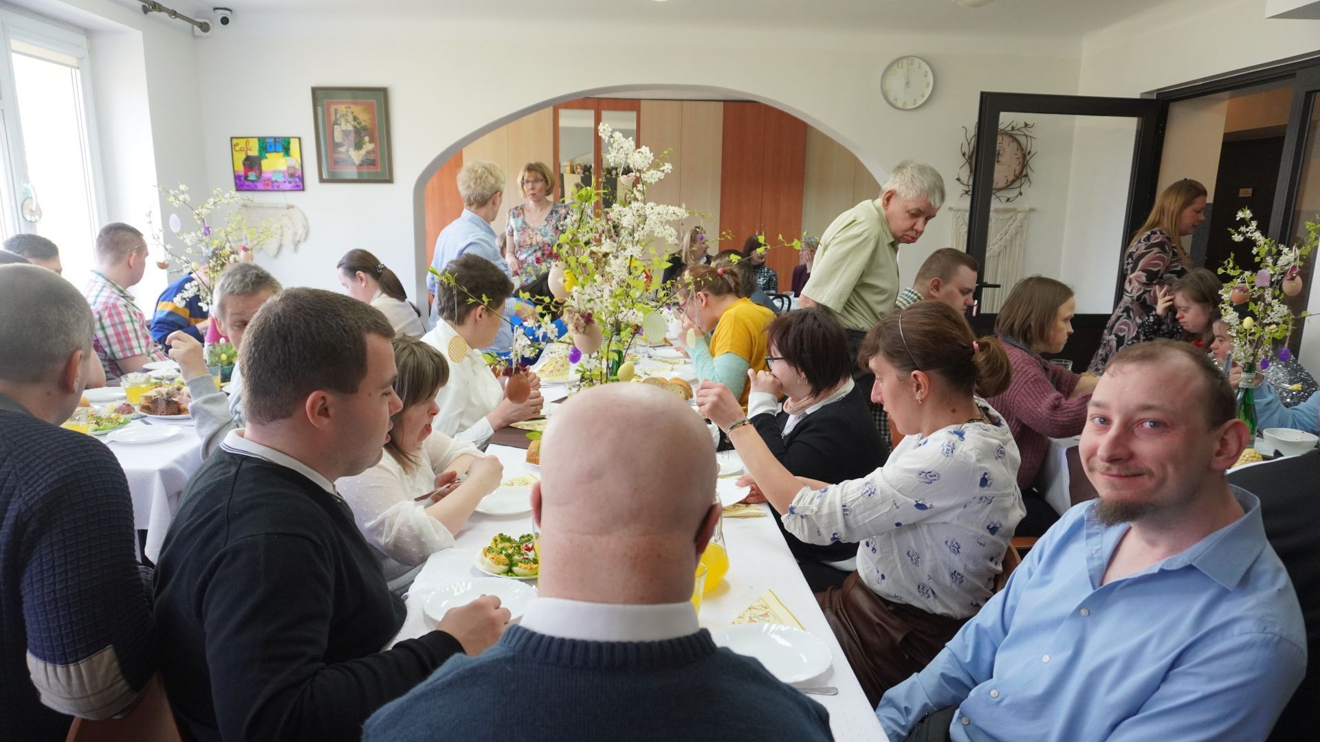 Uczestnicy siedzą przy stołach podczas spotkania wielkanocnego. 