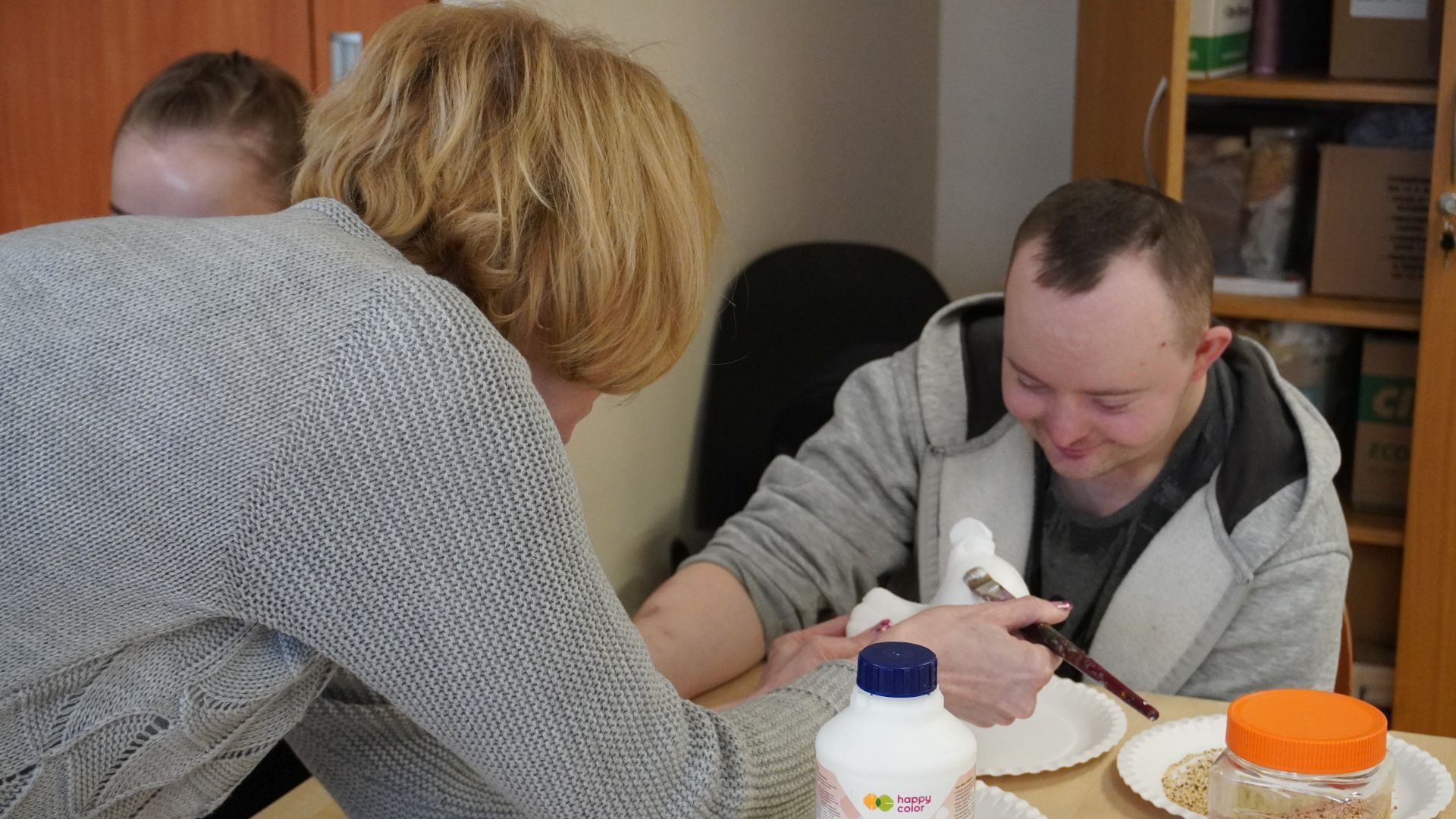 Uczestnik Darek wykonuje ozdobę wielkanocną z pomocą terapeuty.