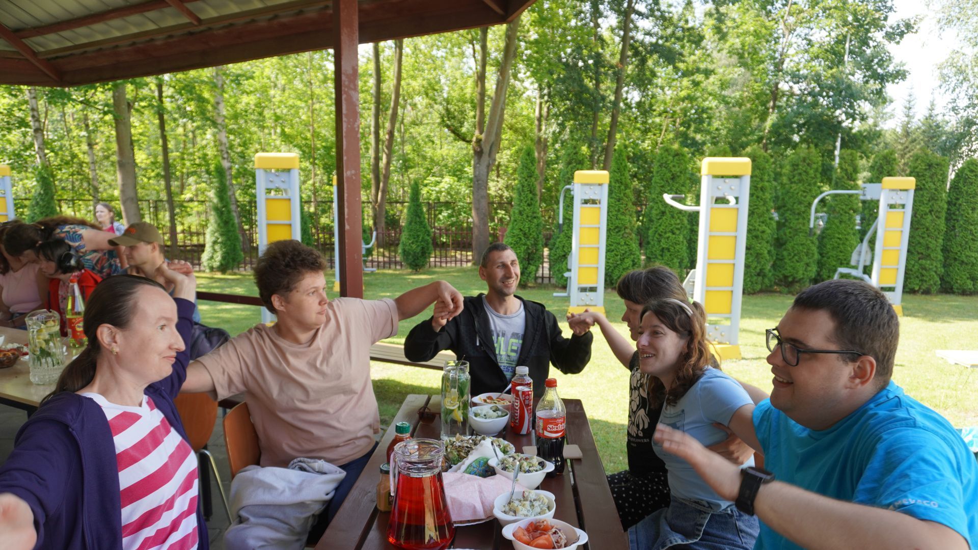 Uczestnicy kołyszący się przy stole w rytm muzyki podczas grilla podsumowującego projekt ''Jesteśmy dla innych''.