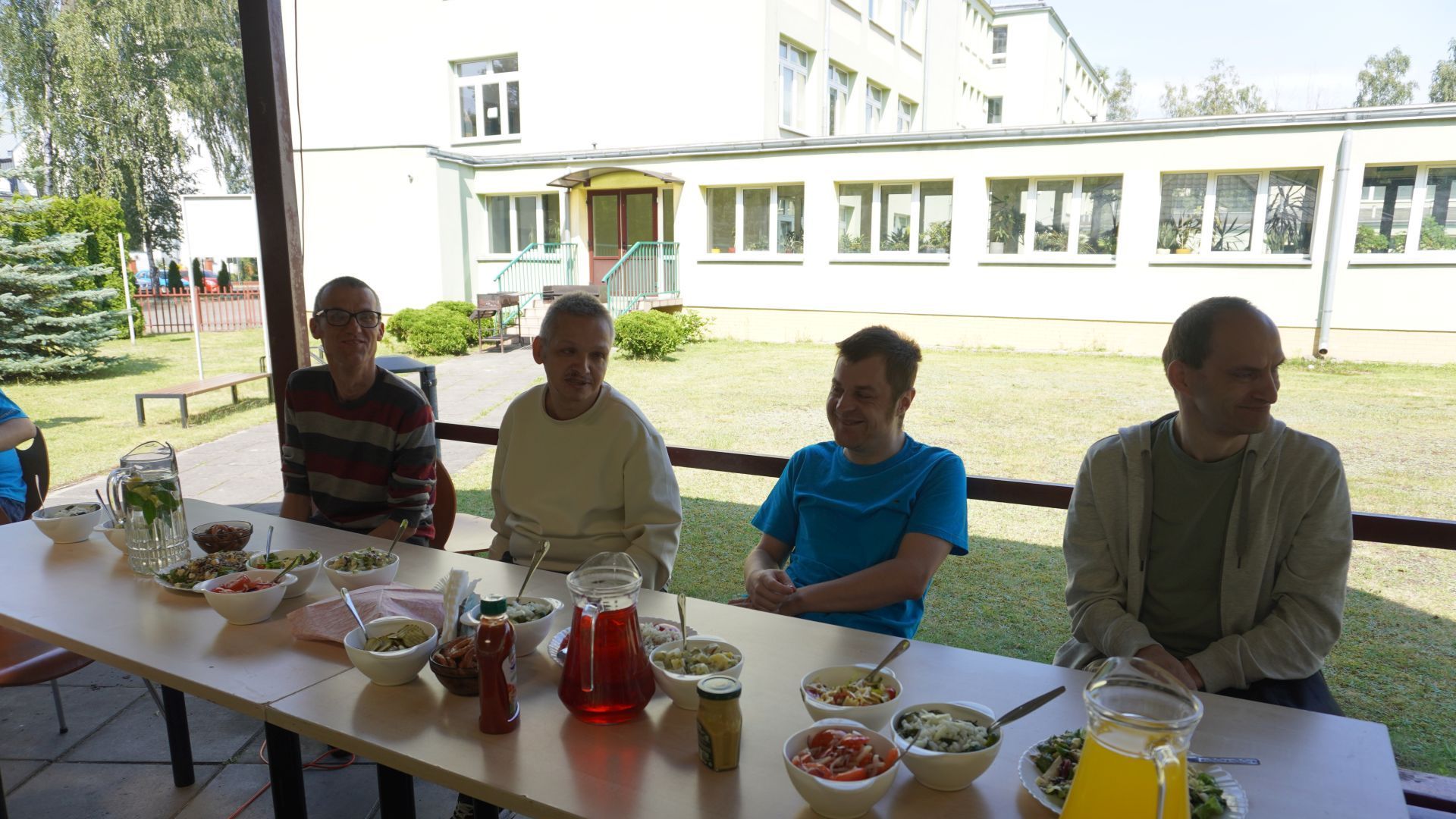 Uczestnicy siedzą przy stole podczas grilla podsumowującego projekt ''Jesteśmy dla innych''.