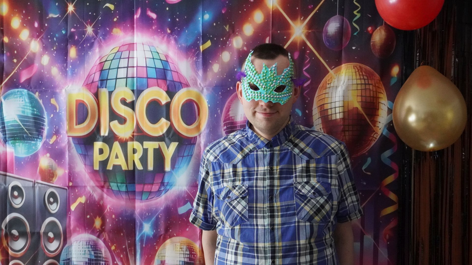 Uczestnik Paweł K. pozuje na ściance zdjęciowej w masce karnawałowej, którą sam wykonał.