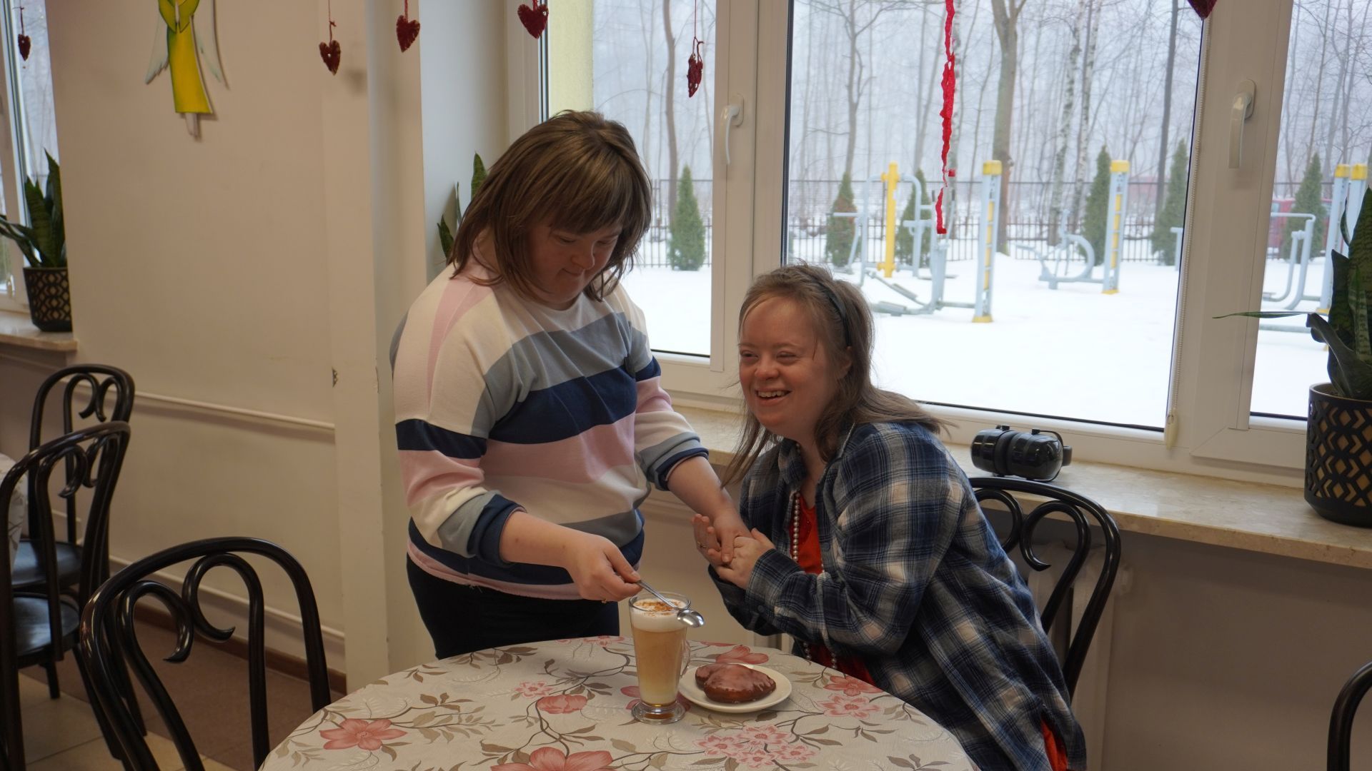 Uczestniczka Sylwia podaje koleżance Martynie do stolika kawę i pączka. 