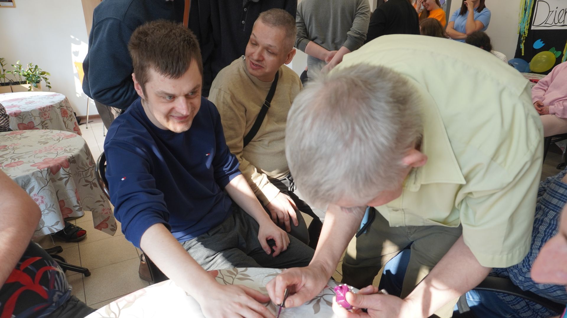 Uczestnik Sławomir maluje koledze Łukaszowi paznokcie podczas zajęć integracyjnych z okazji Dnia Kobiet i Mężczyzn.