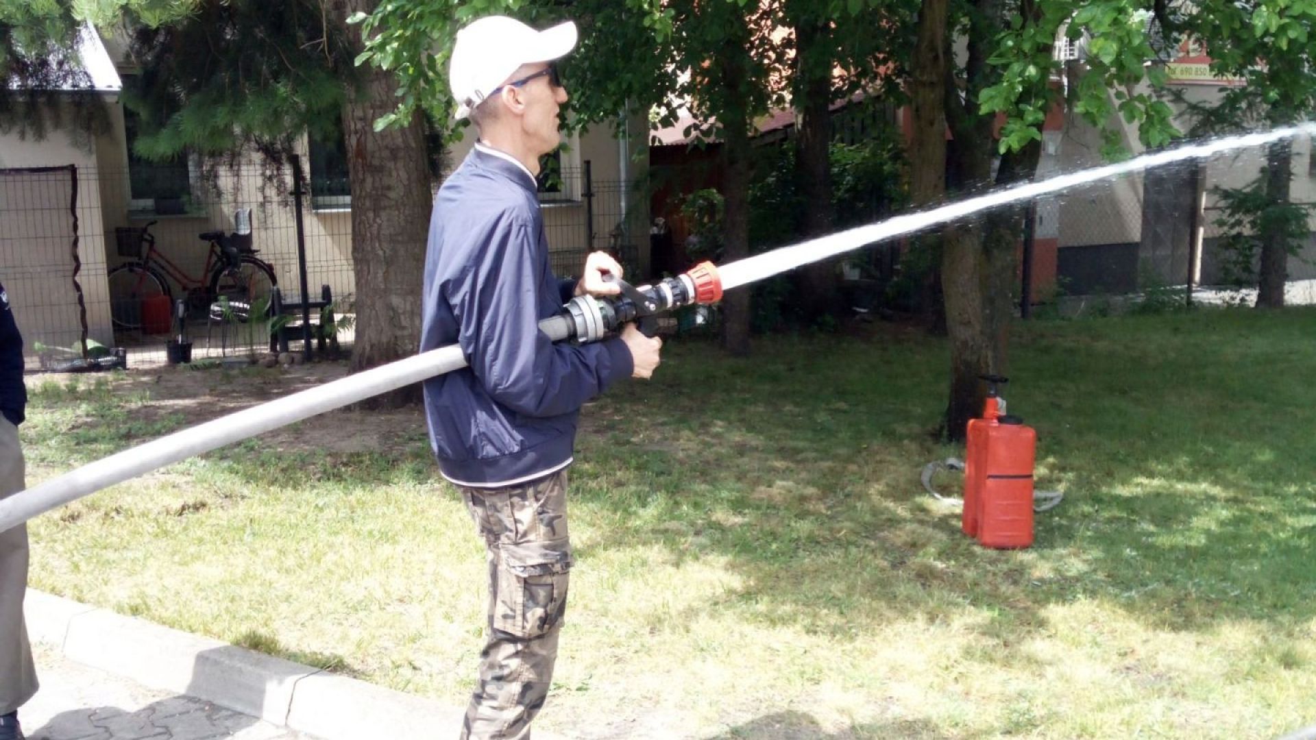 Uczestnik naszego Domu Grzegorz leje wodę z węża strażackiego podczas II Powiatowego Dnia Bezpieczeństwa.