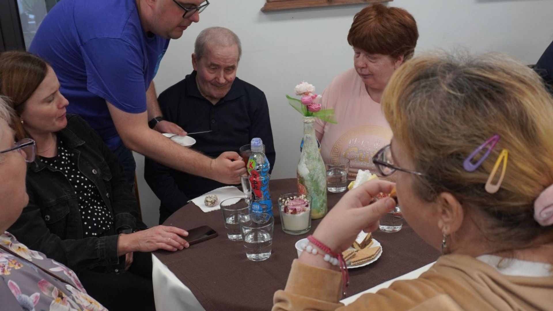 Uczestnik Karol podaje herbatę do stolika podczas warsztatów tworzenia świec w ramach projektu ''Jesteśmy dla innych''.