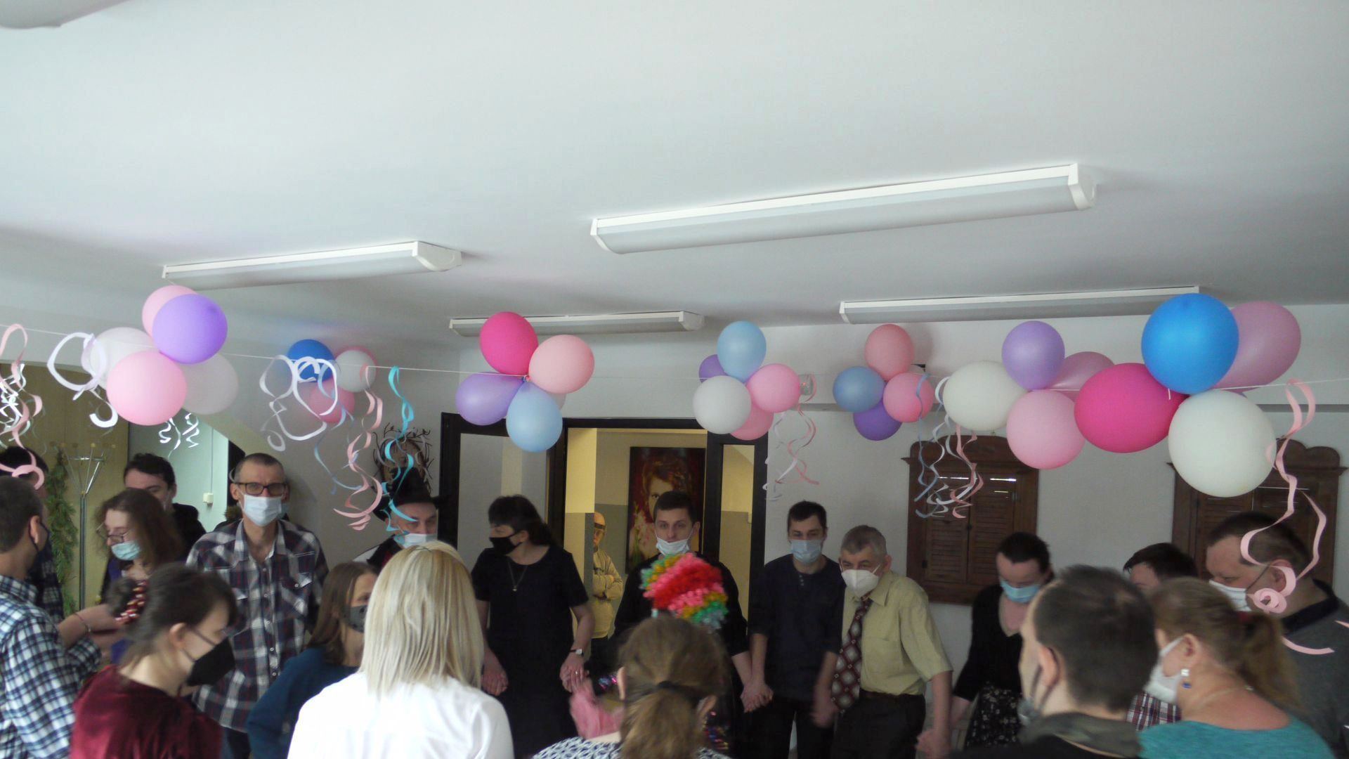 Sala przystrojona balonami, uczestnicy tańczą w kółku trzymając się za ręce.