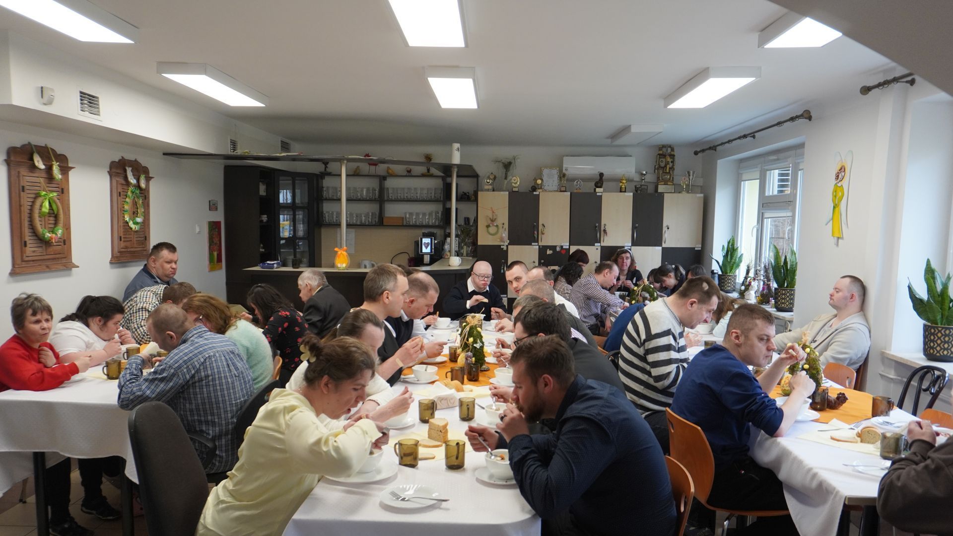 Aktualności: Uczestnicy siedzą przy stołach i jedzą żurek podczas spotkania wielkanocnego.